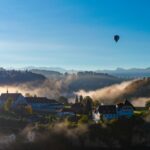 hot air balloon flying over mountain near houses under blue sky